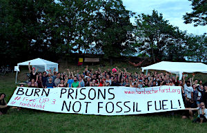 image cropped from Klimacamp 2018 - 121 - 01.06.2018 20-56-19 people in a field with banner: "Burn Prisons not fossil fuels"