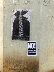 Poster on concrete wall with stencil art of two women facing away from each other, their hair braided together in one braid. Beneath is a poster reading NO! No Trump Pence fascist regime. Stencil posters on a concrete wall, Solidarity graphic, anti fascist art, activist art