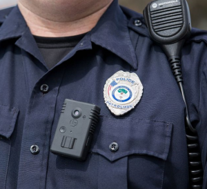 Body camera (Wikimedia Commons) A uniformed cop's upper torso, showing a radio, badge and body camera.