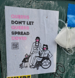 wheatpasted poster with headline "Queers don't let queers spread Covid"; drawing of three people, two adults, one in a wheelchair, all wearing pink respirator masks. The standing adult wears a t-shirt that says "We Keep Us Safe"